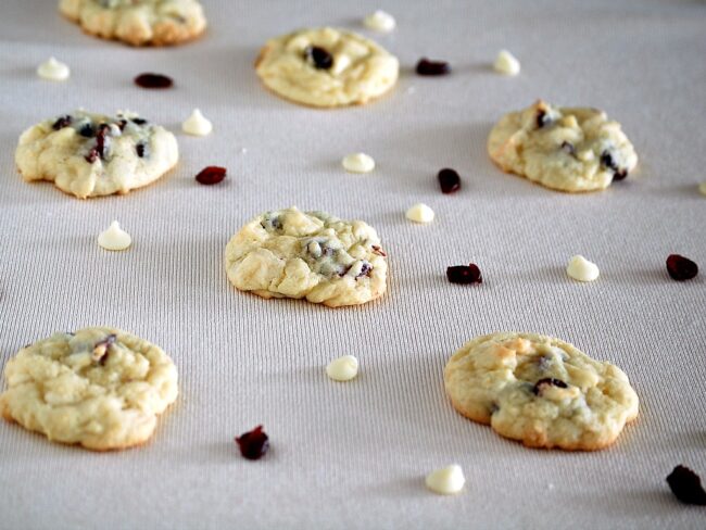 Cranberry white chocolate cookies on an ivory napkin with loose cranberries and white chocolate chips