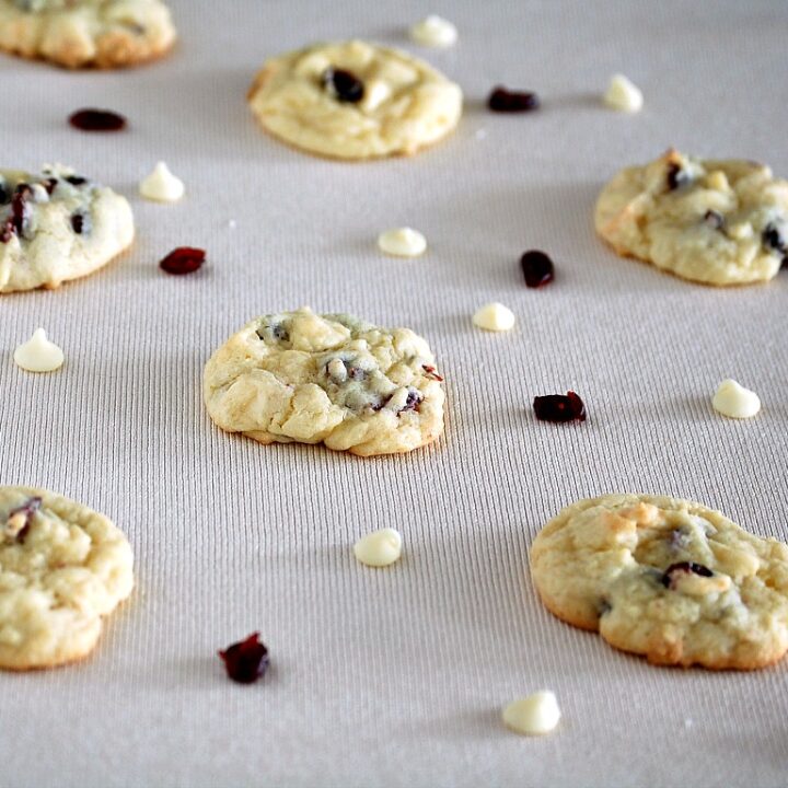 Cranberry white chocolate cookies on an ivory napkin with loose cranberries and white chocolate chips