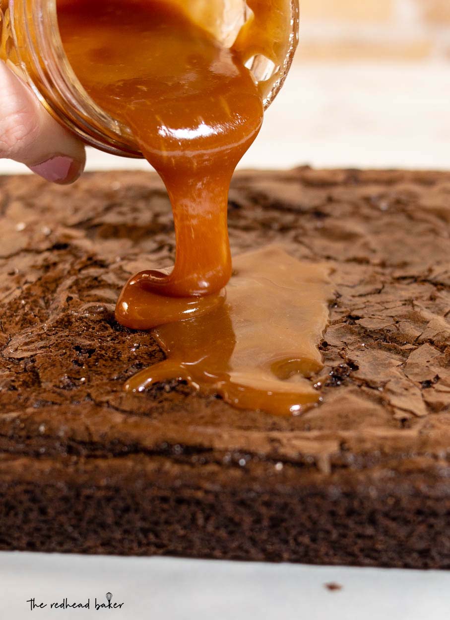 Salted caramel being poured onto a baked sheet of brownies