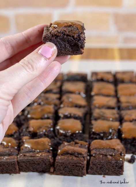 A close-up shot of a square of salted caramel brownie with the rest of the batch in the background