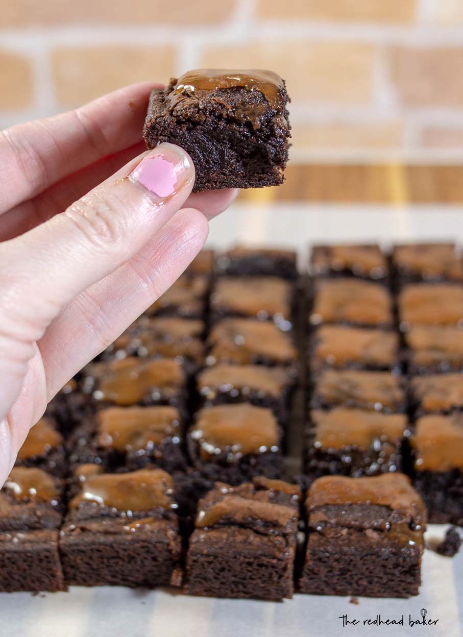 A close-up shot of a square of salted caramel brownie with the rest of the batch in the background