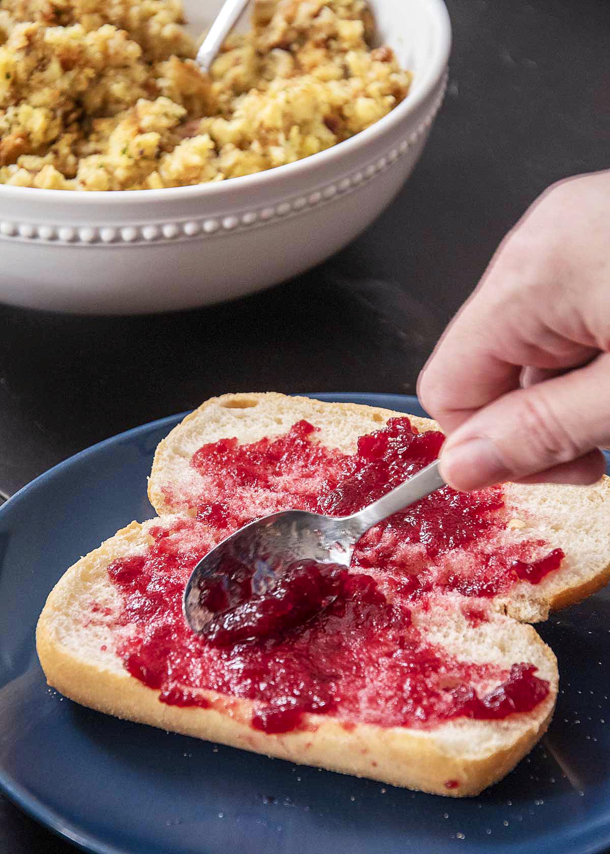 Spreading cranberry sauce on a club roll.