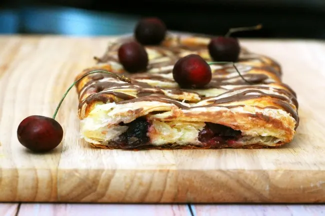 Honor the mothers in your life with this beautiful, decadent cherry cheesecake pastry braid drizzled with chocolate glaze. #SundaySupper theredheadbaker.com