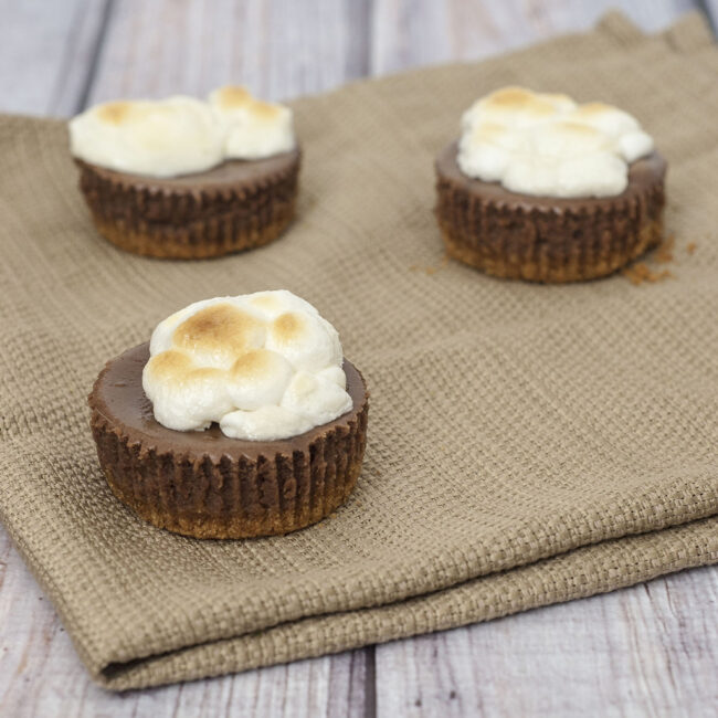 S'mores turn elegant in the form of mini chocolate cheesecakes with graham cracker crusts, topped with marshmallows toasted under the broiler. TheRedheadBaker.com #WhatsBaking