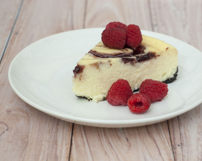 This incredibly rich and creamy white chocolate raspberry cheesecake has swirls of raspberry preserves — it looks difficult, but is to easy to make. #SundaySupper TheRedheadBaker.com