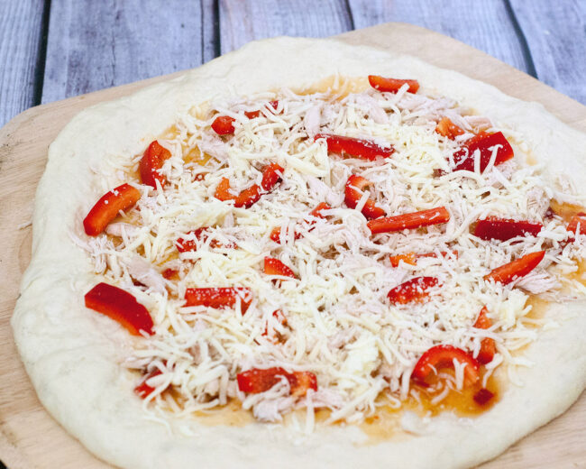 Make an exotic Thai chicken pizza for National Pizza month! Top homemade a pizza crust with sweet Thai sweet chili sauce, shredded chicken and bell peppers. #SundaySupper TheRedheadBaker.com