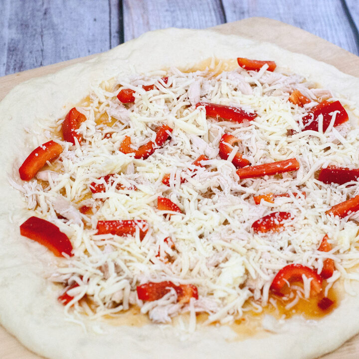 Make an exotic Thai chicken pizza for National Pizza month! Top homemade a pizza crust with sweet Thai sweet chili sauce, shredded chicken and bell peppers. #SundaySupper TheRedheadBaker.com