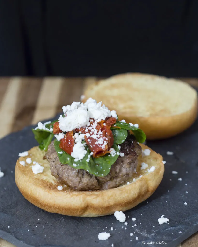 Lamb burgers are flavored with herbs and spices of Greece, then topped with spinach and sun-dried tomatoes tossed with lemon, and a sprinkle of feta. TheRedheadBaker.com