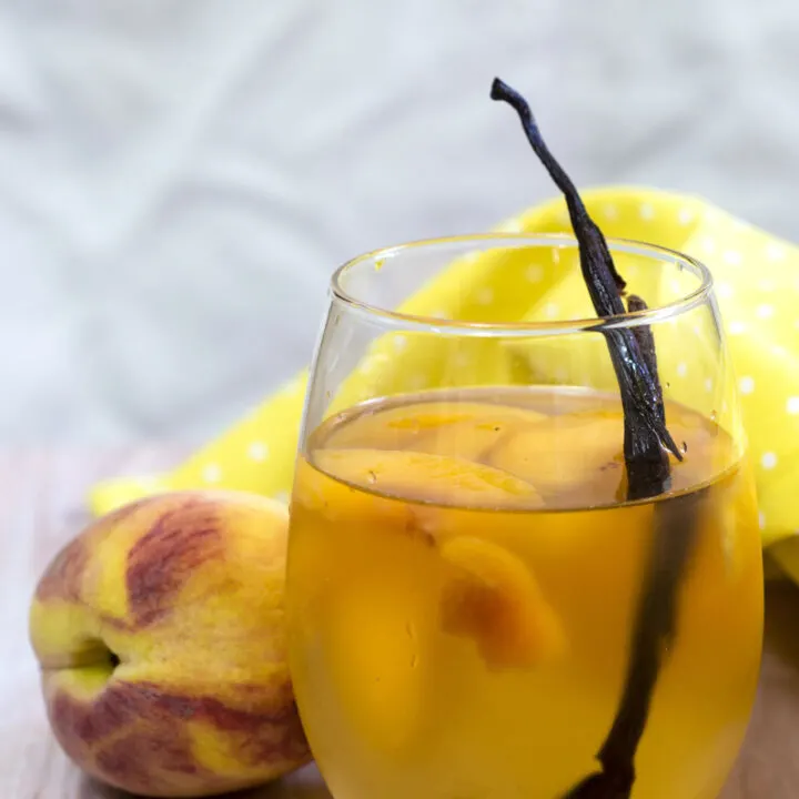 If you try one new cocktail this summer, make it this peach vanilla sangria. Crisp white wine is flavored with peaches, brandy and syrup infused with vanilla bean. #TheRedheadBaker