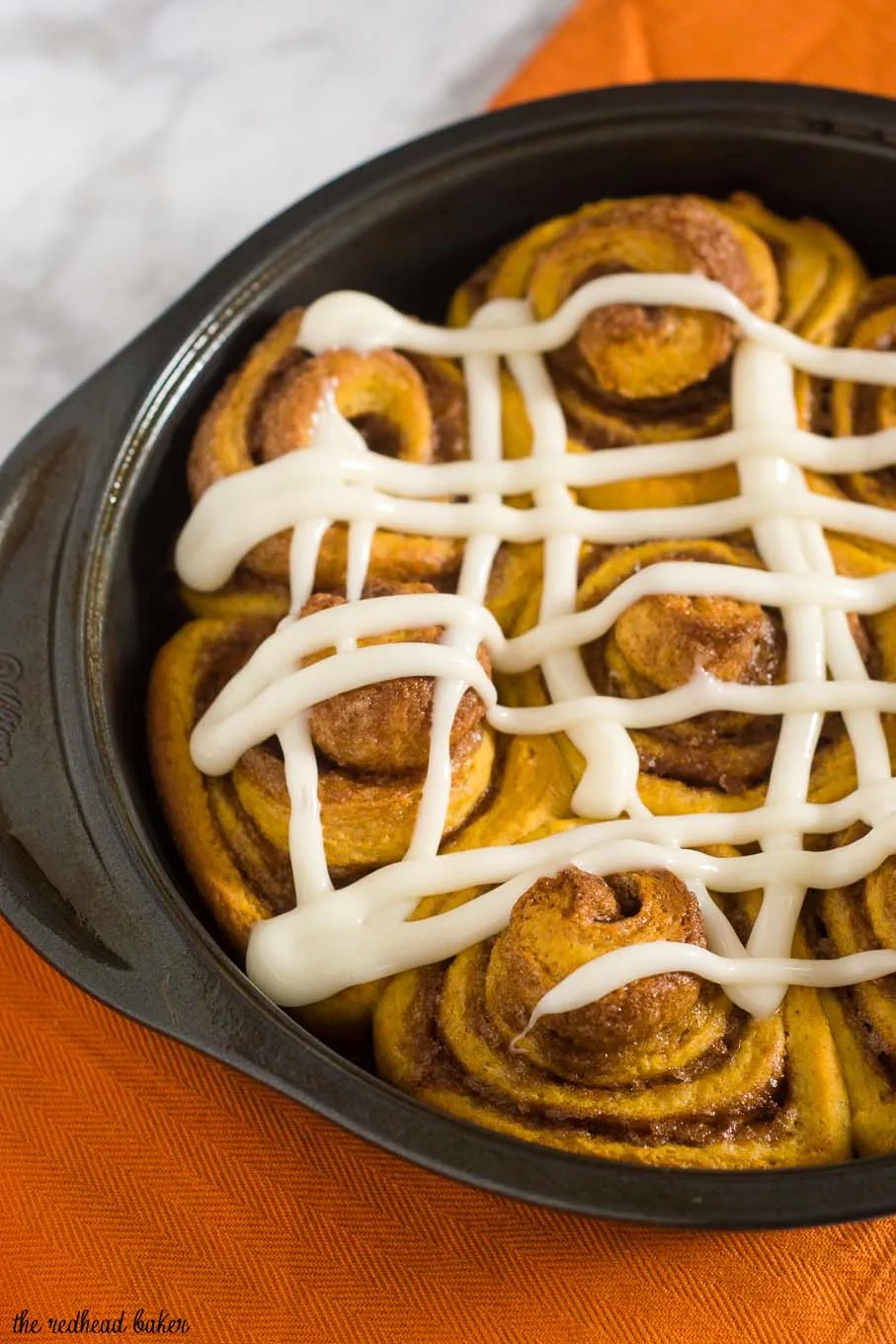 Pumpkin cinnamon rolls are a delicious way to start a fall morning! Sweet dough is flavored with pumpkin, rolled with a cinnamon filling, and topped with cream cheese drizzle. #PumpkinWeek