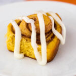 Pumpkin cinnamon rolls are a delicious way to start a fall morning! Sweet dough is flavored with pumpkin, rolled with a cinnamon filling, and topped with cream cheese drizzle. #PumpkinWeek