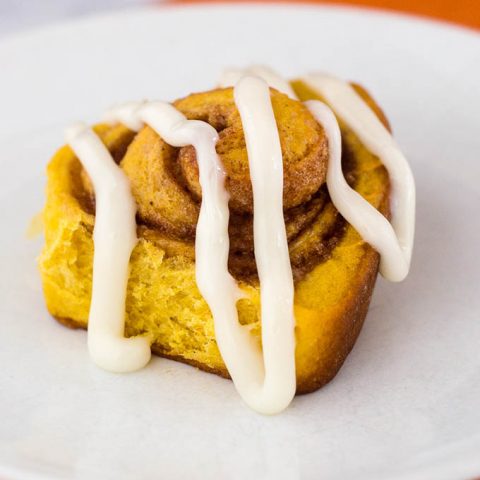 Pumpkin cinnamon rolls are a delicious way to start a fall morning! Sweet dough is flavored with pumpkin, rolled with a cinnamon filling, and topped with cream cheese drizzle. #PumpkinWeek