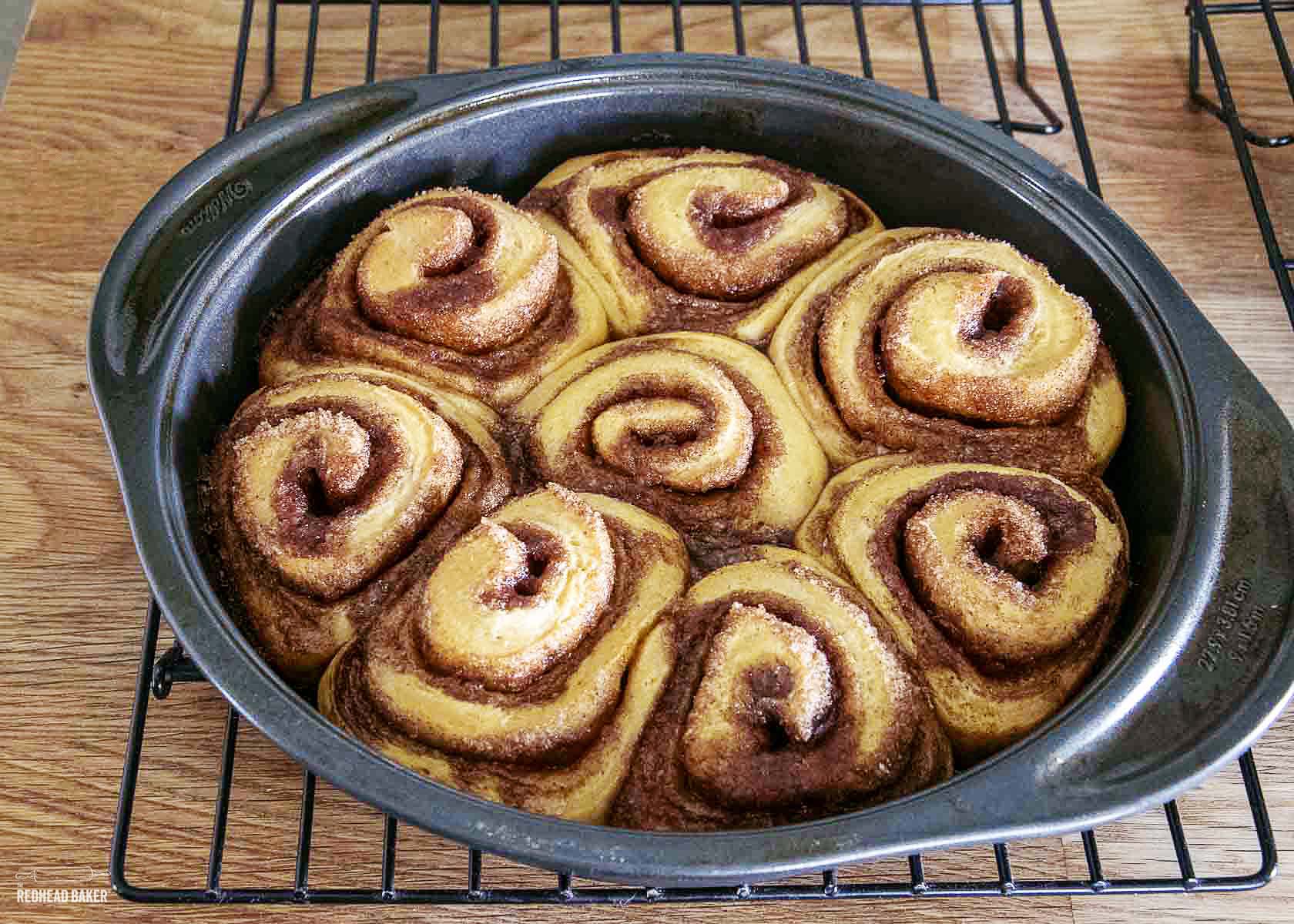 A pan of baked cinnamon rolls on a wire cooling rack. 
