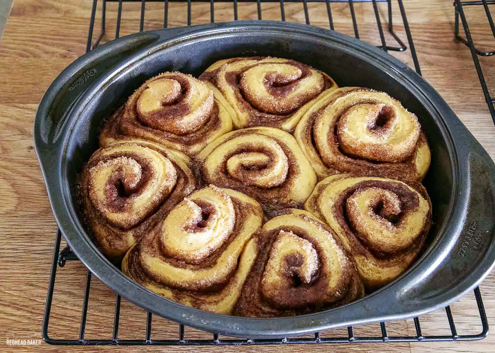 A pan of baked cinnamon rolls on a wire cooling rack.