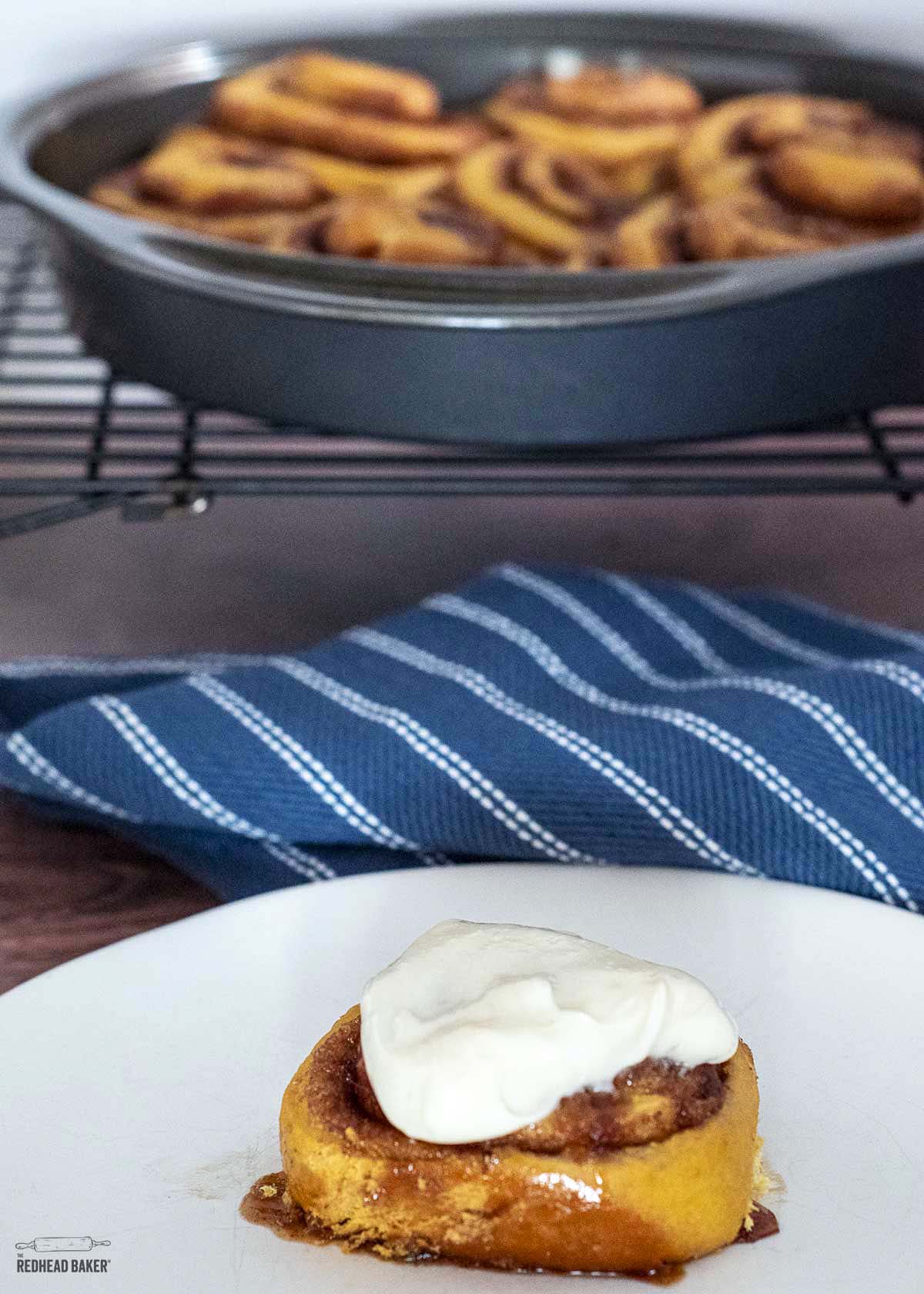 A cinnamon roll in front of a pan of baked cinnamon rolls. 