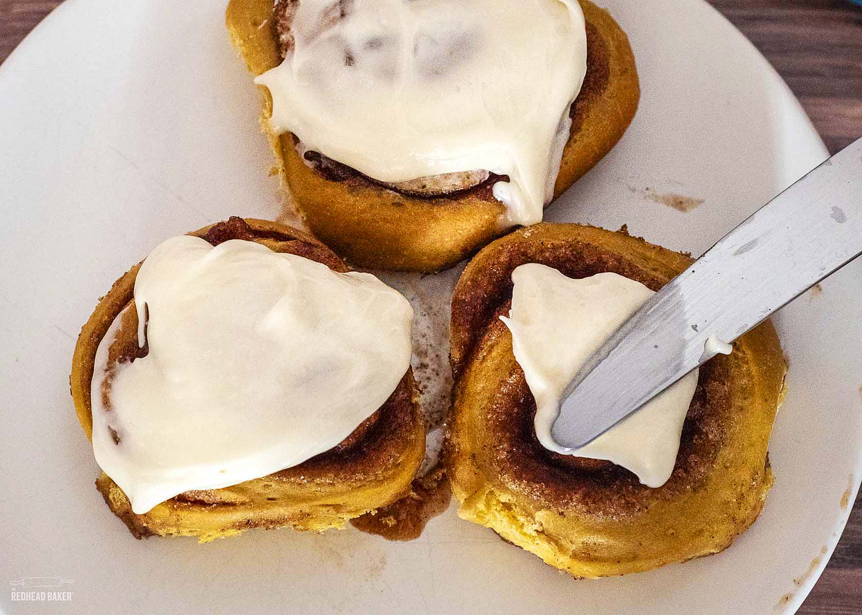 Icing being spread on a baked cinnamon roll. 
