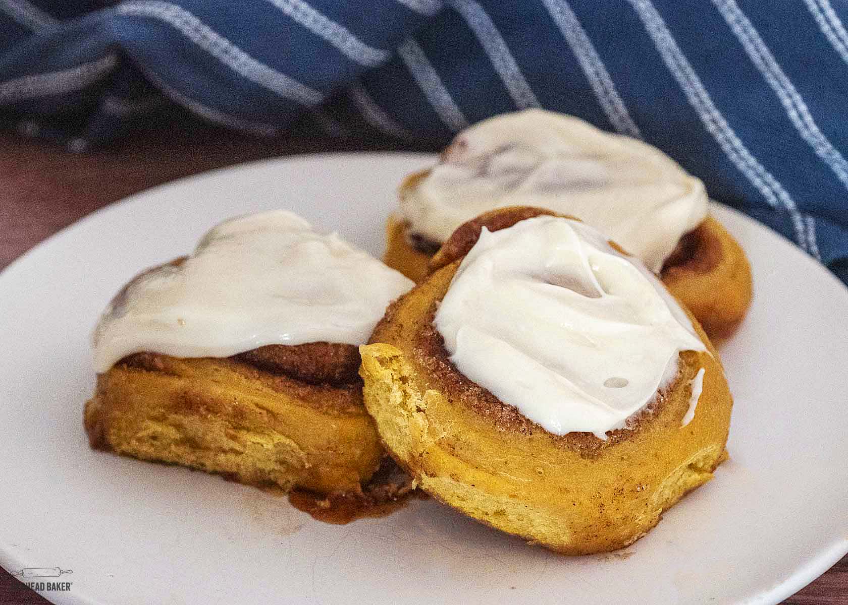 Three iced pumpkin cinnamon rolls on a white plate. 