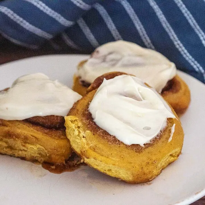 Three iced pumpkin cinnamon rolls on a white plate.