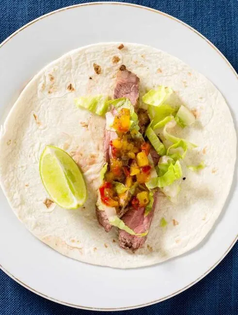 Flank steak tacos use a lean cut of beef, tenderized with a chile-lime marinade, as taco filling in soft tortillas, topped with shredded lettuce and pineapple salsa. #SundaySupper