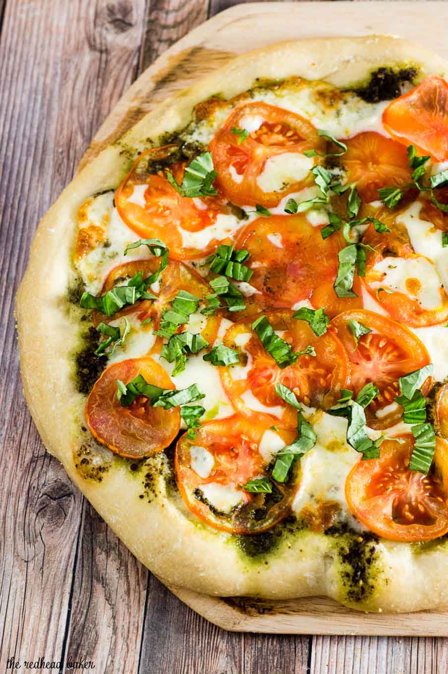 Caprese pizza is topped with pesto, thinly sliced tomatoes, and mozzarella cheese. Fresh basil and a balsamic glaze are added after baking.