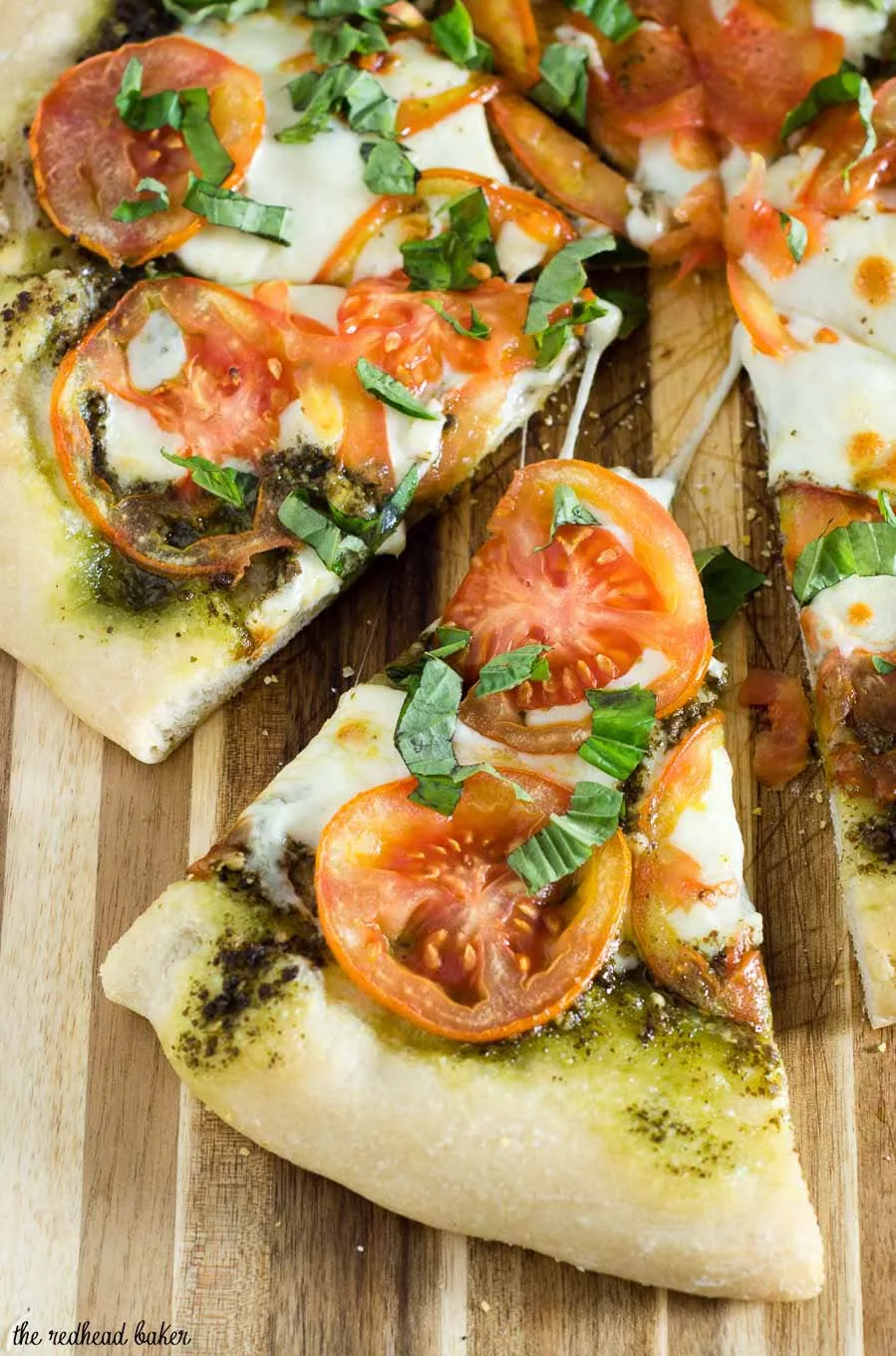 Caprese pizza is topped with pesto, thinly sliced tomatoes, and mozzarella cheese. Fresh basil and a balsamic glaze are added after baking.