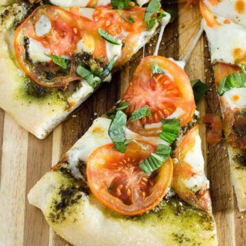 Caprese pizza is topped with pesto, thinly sliced tomatoes, and mozzarella cheese. Fresh basil and a balsamic glaze are added after baking.