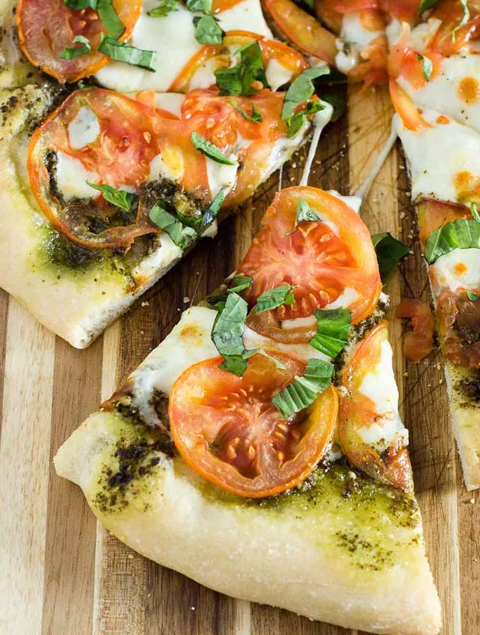 Caprese pizza is topped with pesto, thinly sliced tomatoes, and mozzarella cheese. Fresh basil and a balsamic glaze are added after baking.