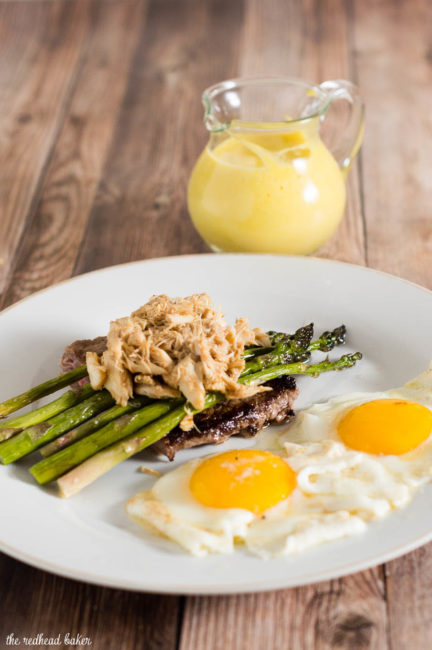 The classic brunch staple of steak and eggs gets fancy! The steak is served Oscar-style with asparagus, crab meat and Hollandaise sauce, with two sunny side-up eggs. #BrunchWeek