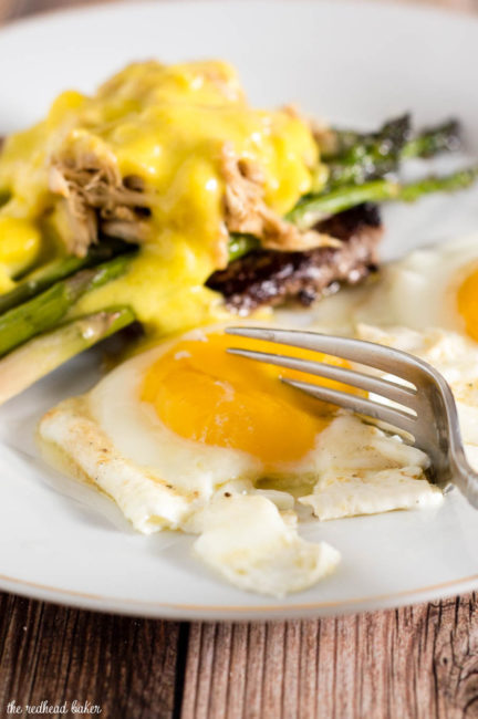 The classic brunch staple of steak and eggs gets fancy! The steak is served Oscar-style with asparagus, crab meat and Hollandaise sauce, with two sunny side-up eggs. #BrunchWeek