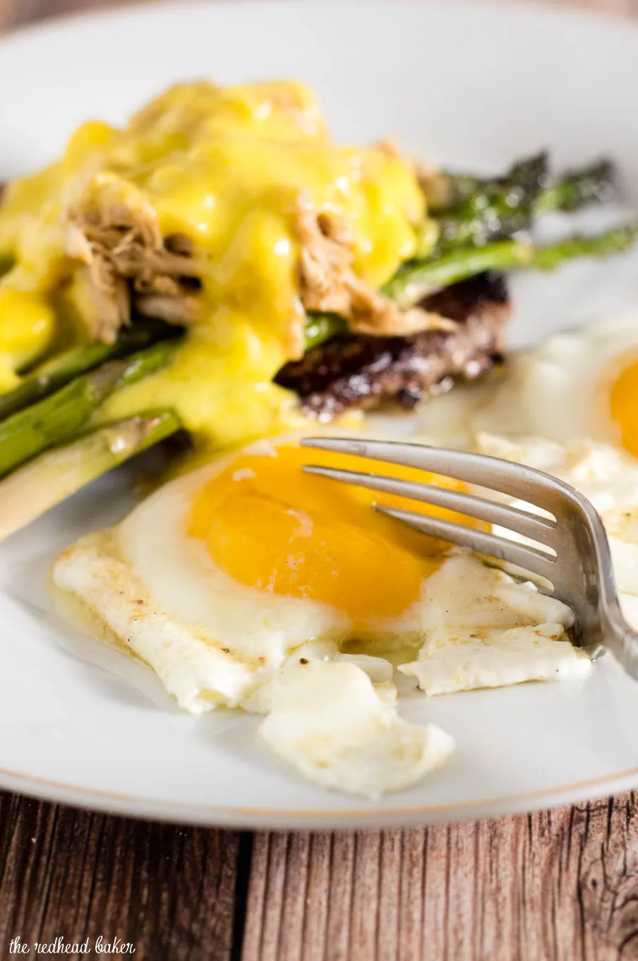 The classic brunch staple of steak and eggs gets fancy! The steak is served Oscar-style with asparagus, crab meat and Hollandaise sauce, with two sunny side-up eggs. #BrunchWeek