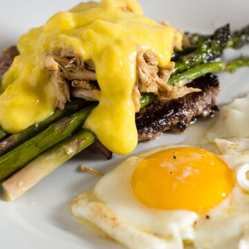 The classic brunch staple of steak and eggs gets fancy! The steak is served Oscar-style with asparagus, crab meat and Hollandaise sauce, with two sunny side-up eggs. #BrunchWeek