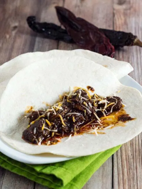 Authentic barbacoa beef tacos are piled with shredded beef cooked low and slow in chili-pepper spiced sauce, and topped with cilantro, salsa and lime wedges.