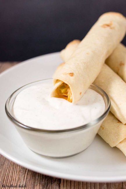 A baked buffalo chicken taquito being dipped in ranch sauce.