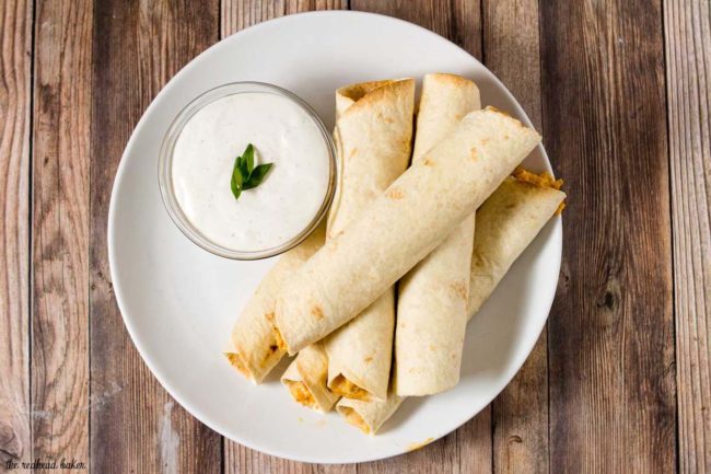 A plate of baked buffalo chicken taquitos and ranch dipping sauce.