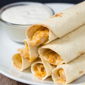 A plate of baked buffalo chicken taquitos and ranch dipping sauce.