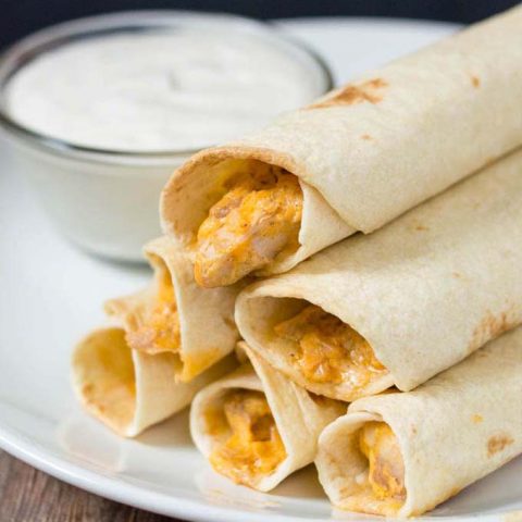 A plate of baked buffalo chicken taquitos and ranch dipping sauce.