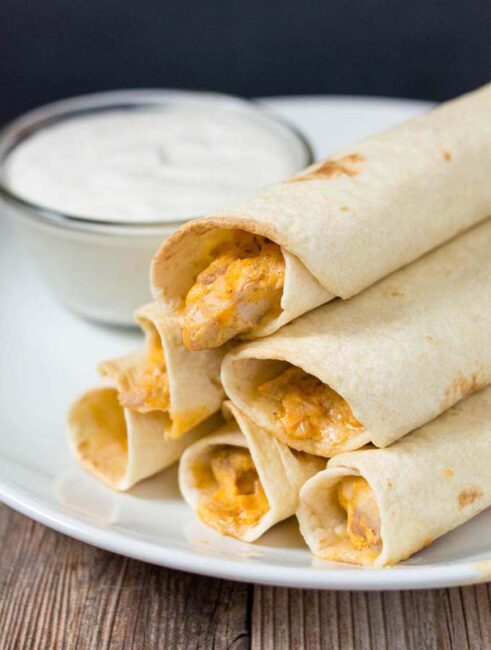 A plate of baked buffalo chicken taquitos and ranch dipping sauce.