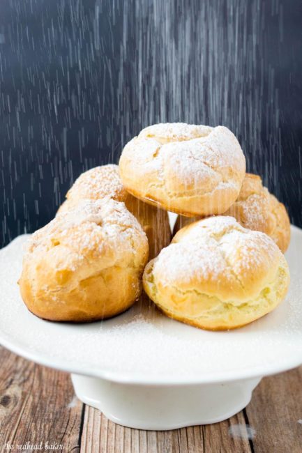 A plate of cannoli cream puffs being dusted with powdered sugar.