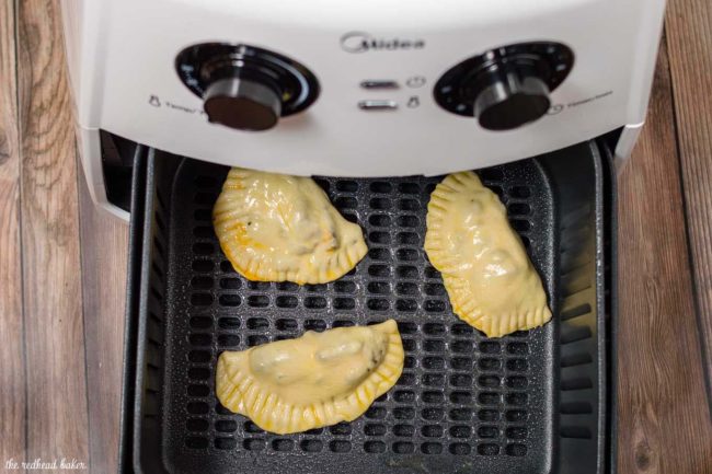 Un-cooked Philly cheesesteak empanadas in the basket of the air-fryer.