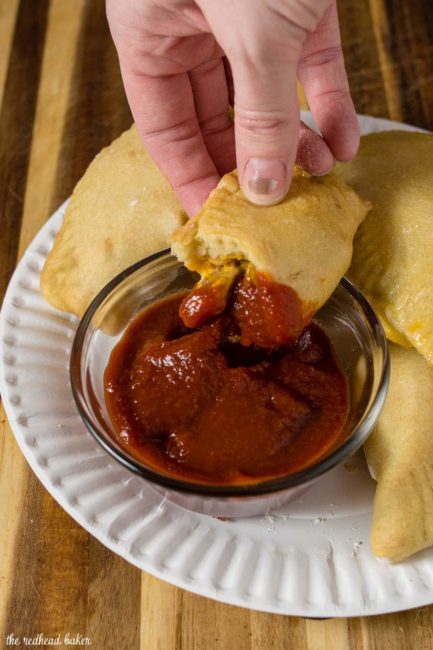 Half of a Philly Cheesesteak Empanada being dipped in the Red Duck Smoky Ketchup dipping sauce.