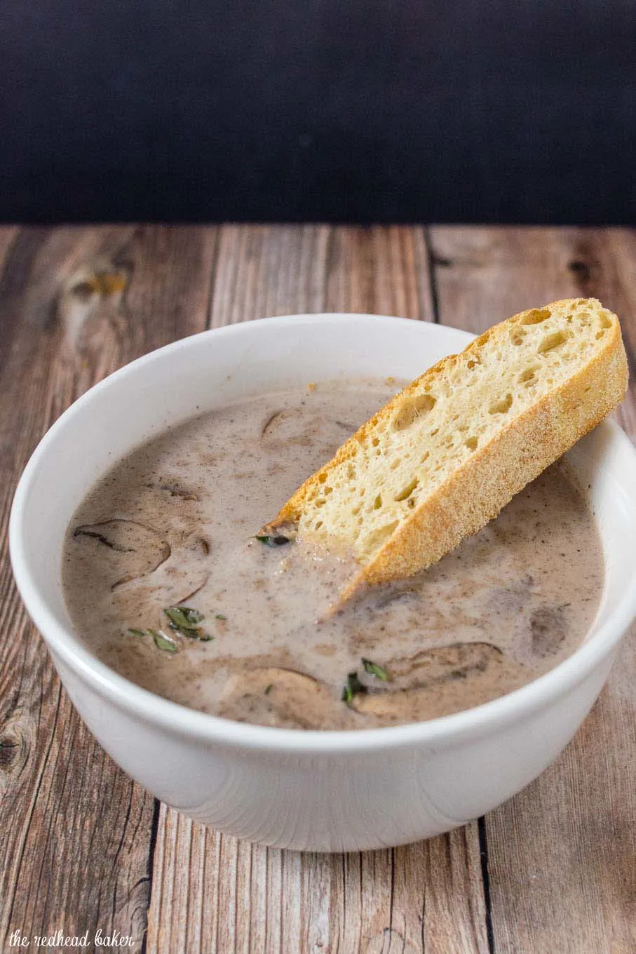 A piece of ciabatta bread being dipped in a bowl of port wine cream of mushroom soup