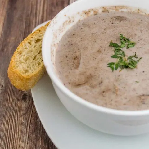 A bowl of port wine cream of mushroom soup with a stick of ciabatta bread on the side