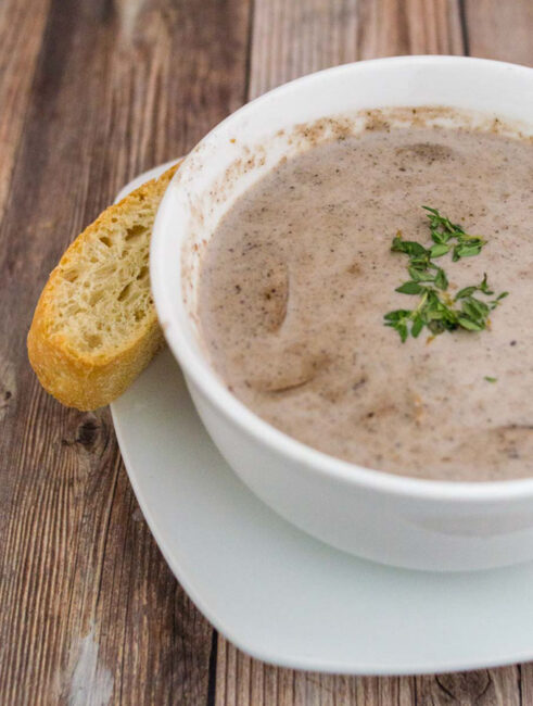 A bowl of port wine cream of mushroom soup with a stick of ciabatta bread on the side