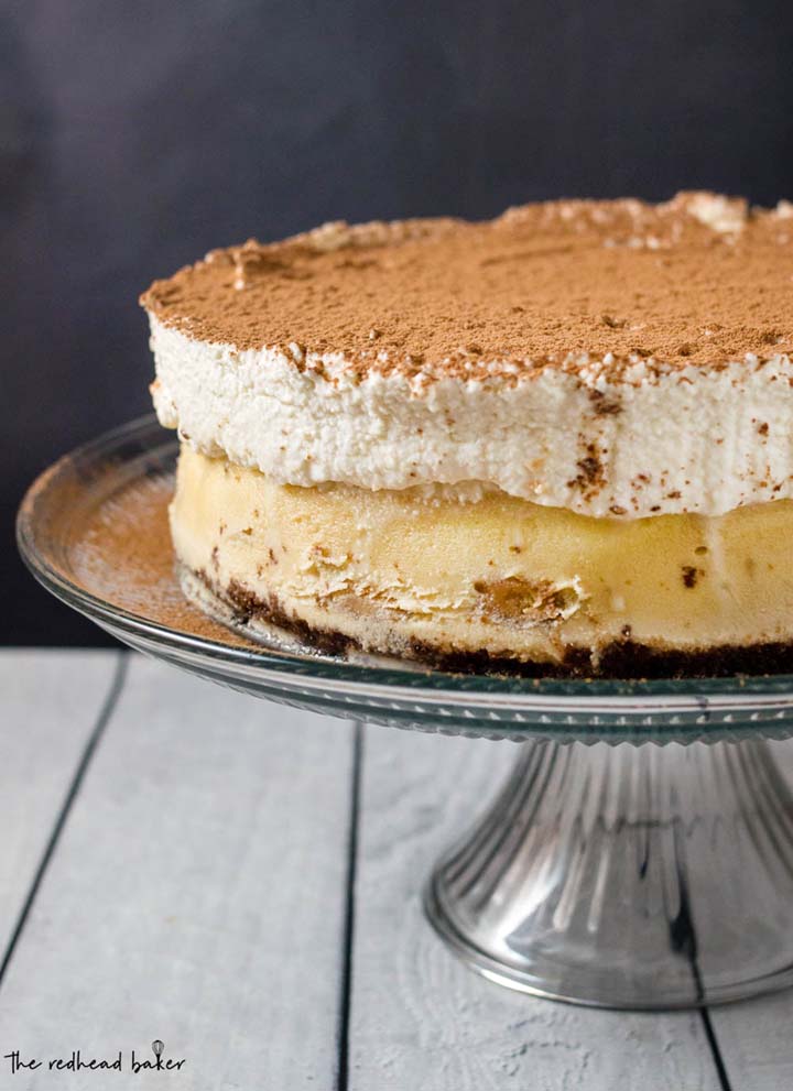 Tiramisu cheesecake on a glass cake stand.