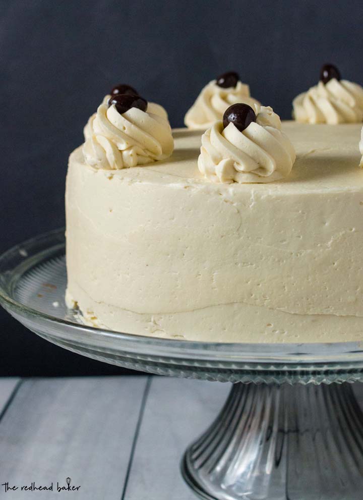 A whole, uncut white chocolate mocha layer cake on a glass cake stand.