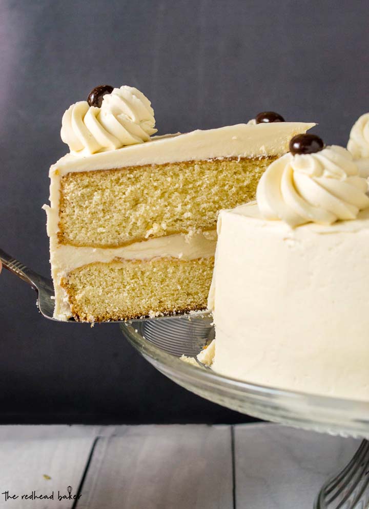 A slice of white chocolate mocha layer cake being lifted off the glass cake stand.