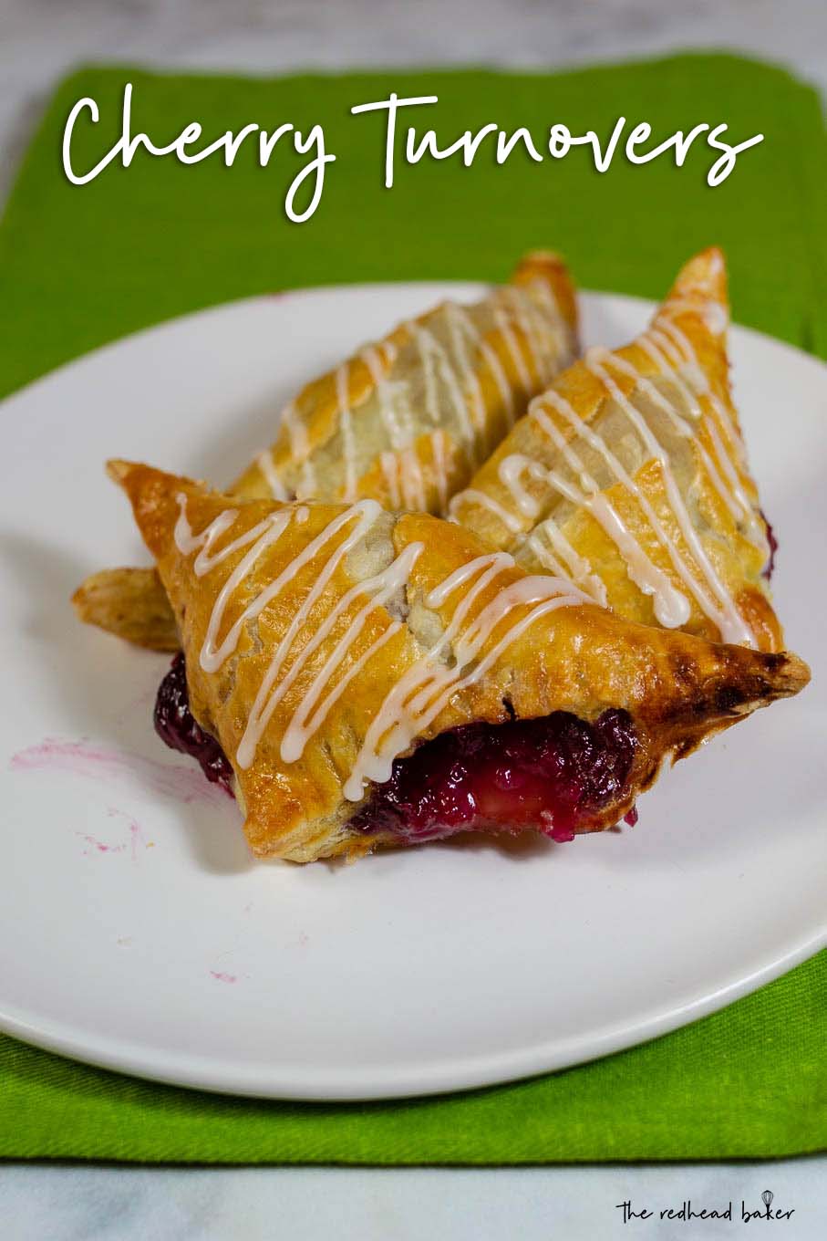 Three cherry turnovers on a plate, on top of a green tea towel