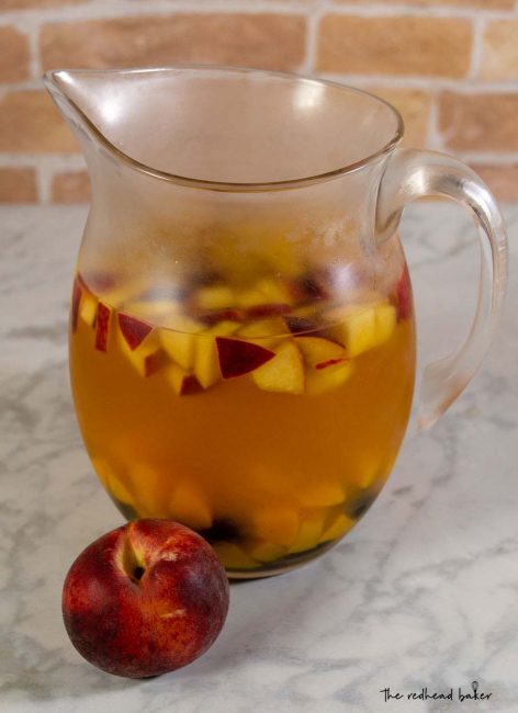 A pitcher of sparkling peach blackberry sangria with a whole fresh peach.