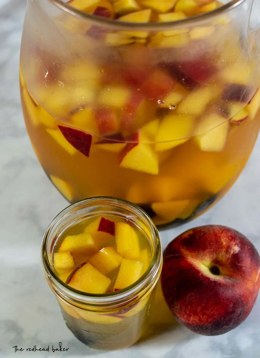 An overhead shot of a glass of sparkling blackberry peach sangria, the pitcher and a fresh peach.