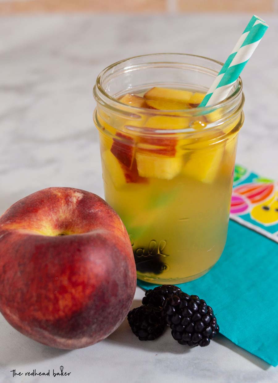 A close-up shot of a glass of sparkling blackberry peach sangria, a fresh peach, and 3 blackberries